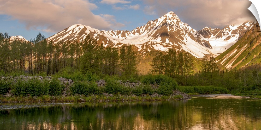 Landscape photograph of a lake in front of snowy mountain peaks with warm lighting.