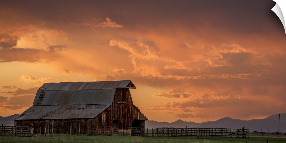 A photograph of an old barn under illuminated clouds of a sunset.