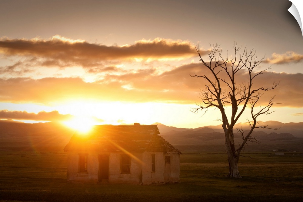 Landscape photograph of an old abandoned house in a field with mountains in the background and the sun shining right on th...