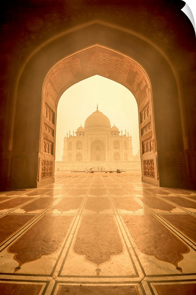 View of the Taj Mahal through a detailed archway with golden sun shining in.