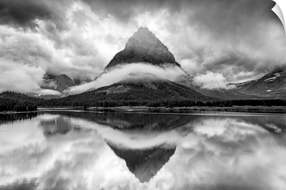 A black and white photograph of a pointed mountain surrounded by a ribbon of cloud while casting a perfect reflection in t...