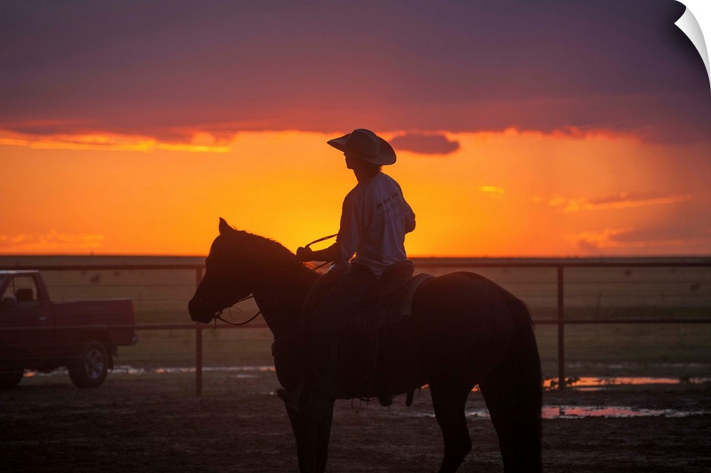 Silhouette photograph of a cowboy on horseback with a beautiful purple and orange sunset in the background.