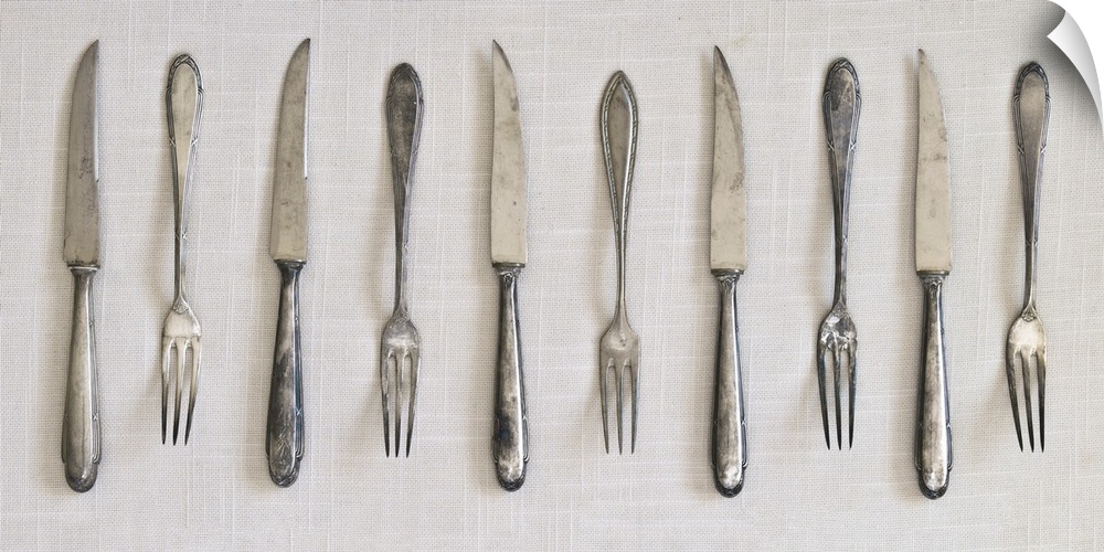 Photograph of a row of silver antique forks and knifes on a linen cloth.