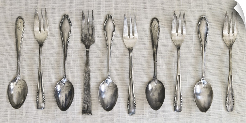 Photograph of a row of silver antique forks and spoons on a linen cloth.