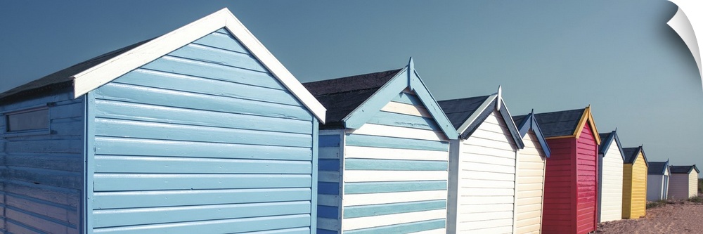 A panoramic image of a long line of colorful beach huts on a clear day.