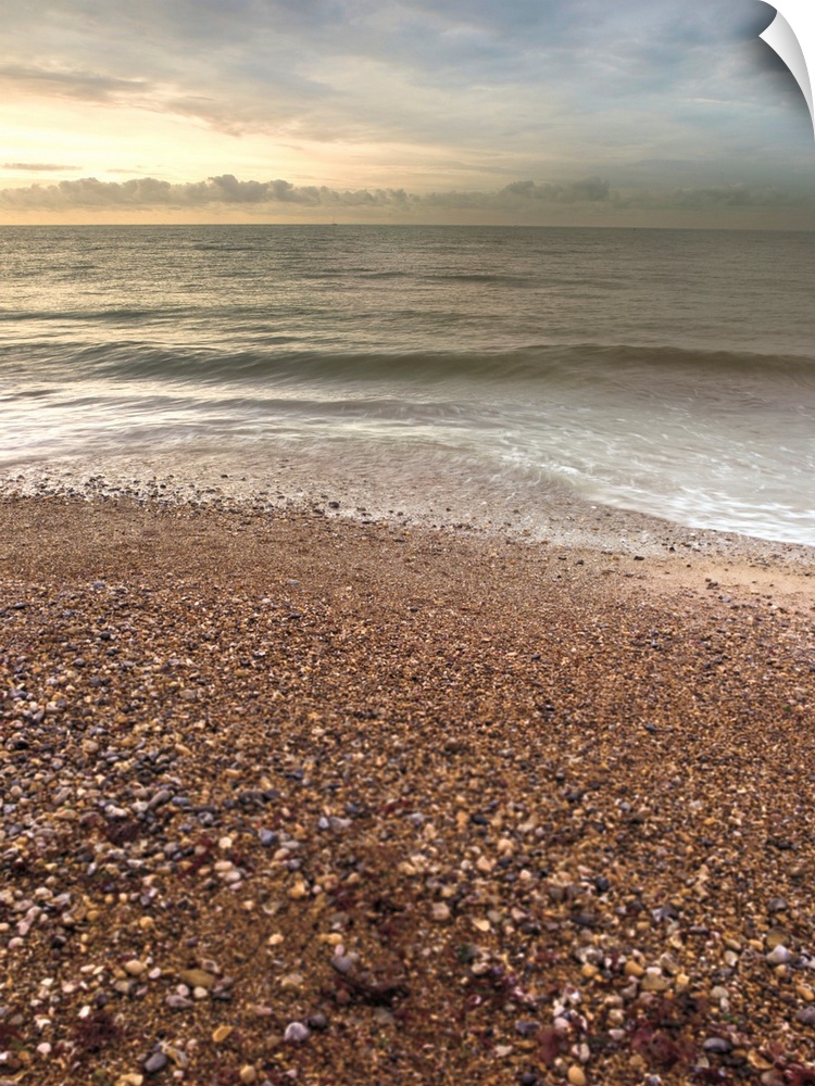 Vertical photograph of a pebble covered beach with gentle waves.
