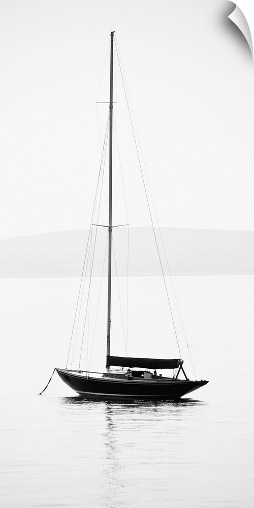 Black and white photograph of a sailboat with its sail down on calm water.