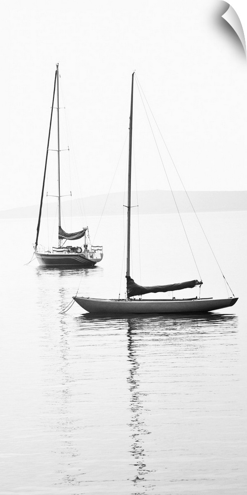 Black and white photograph of two sailboats with sails down on calm water.