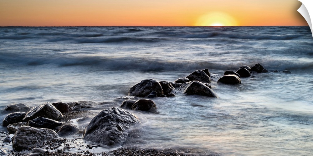 Photograph of a line of rocks in the surf of a beach during sunset.