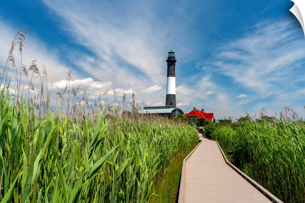 USA, New York, Long Island, wooden path to the Fire Island Lighthouse surrounded by beach grass, blue sky, white clouds.