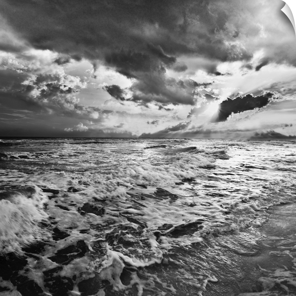 A black and white image of the sea with crashing waves on the beach.