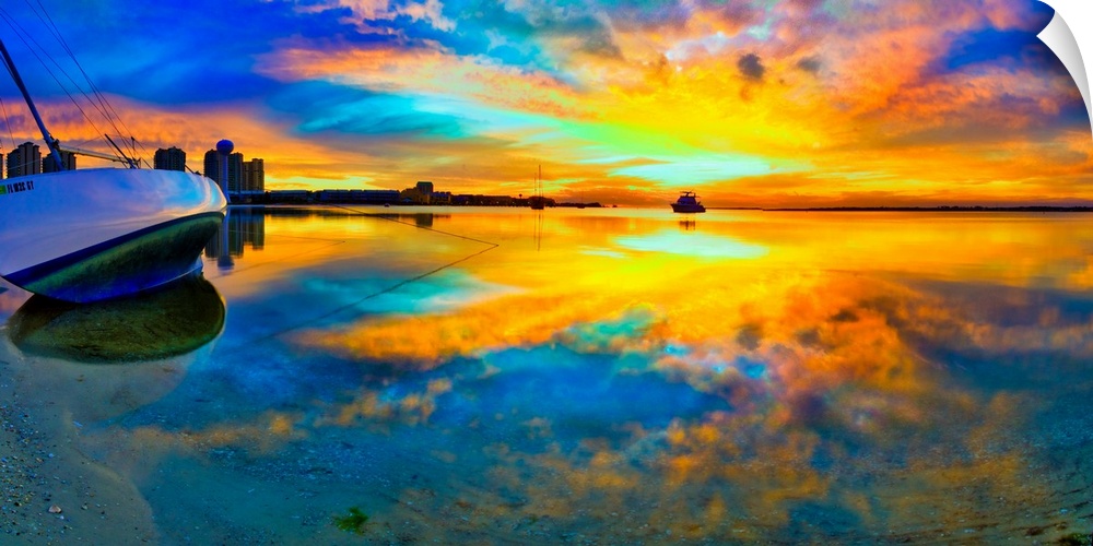 A panoramic beach sunset with a burning bright reflection in the water. Yellow and blue sky reflecting in water and a boat...