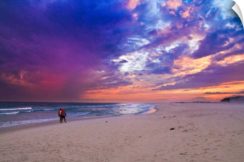 People walking on the beach during a pink and purple sunset along the Gulf Islands National Seashore.