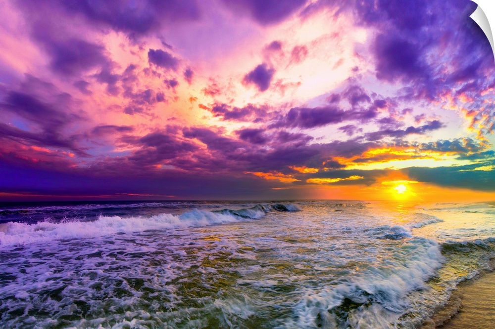 A beach sunset with beautiful pink and purple clouds. The ocean is littered with foamy waves under the pink sunset.