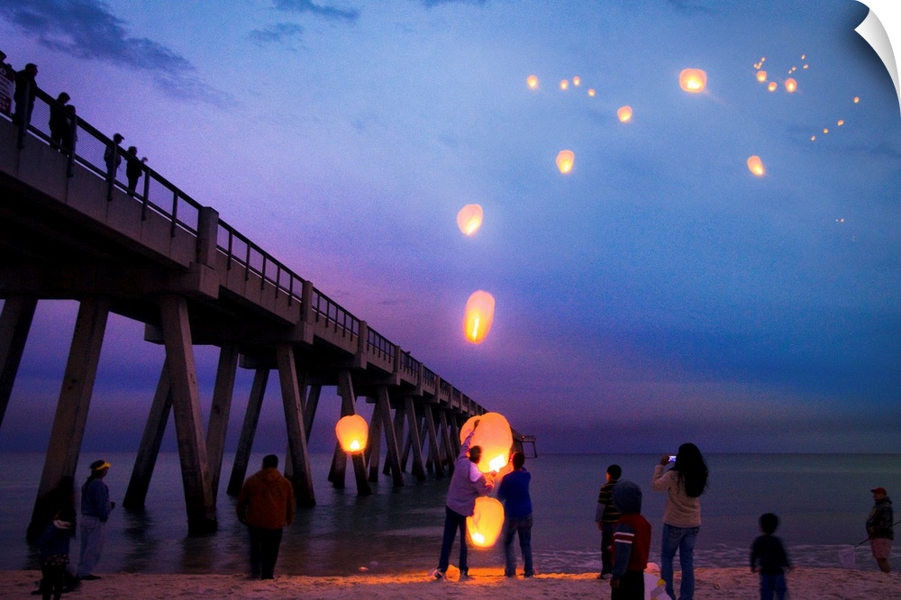 Blue seascape with people releasing paper lanterns over the sea.