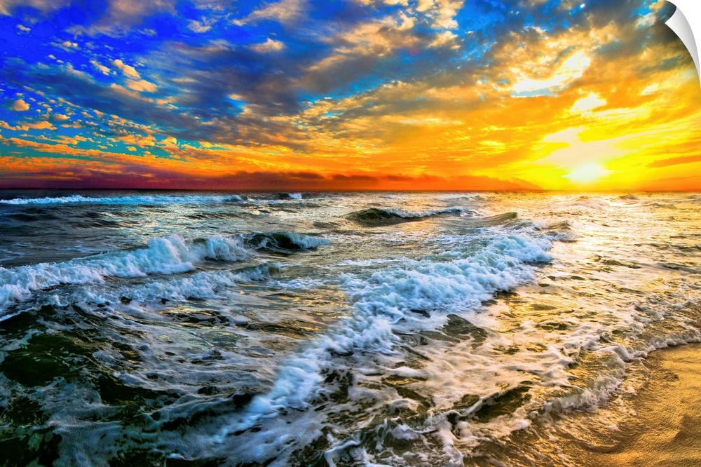 Beautiful ocean waves roll in front of a yellow orange and blue sunset. The sunset goes down into the beautiful blue ocean.