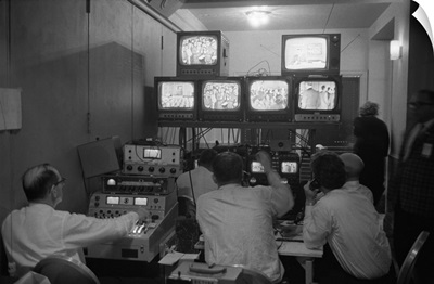 Broadcasting technicians, seated in front of bank of television sets