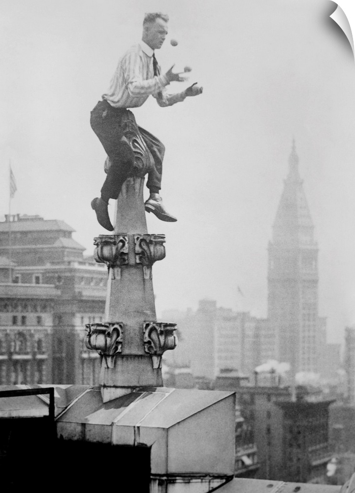 Human Fly' John 'Jammie' Reynolds juggles while balancing atop a roof decoration in New York City. In the distance is the ...