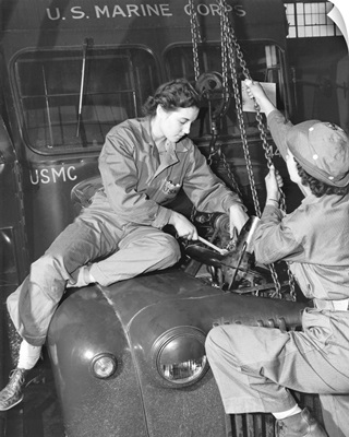 Women Marines lower a reconditioned engine back in place in a Marine Corps bus