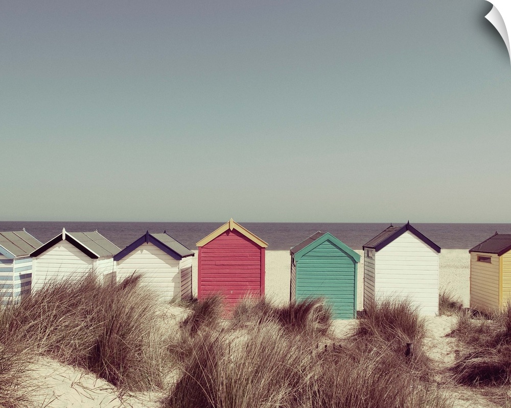 A photograph of multi-colored cottages lined up in a row on the beach.