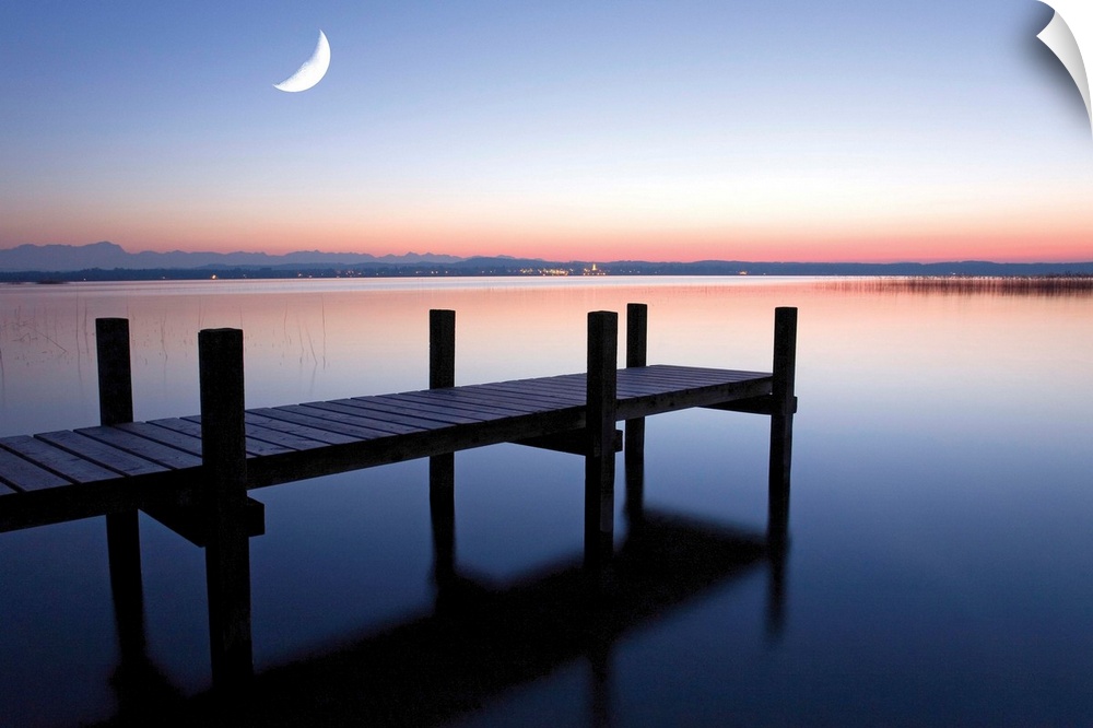 Sunset photograph of a dock over calm water and a half moon in the sky.