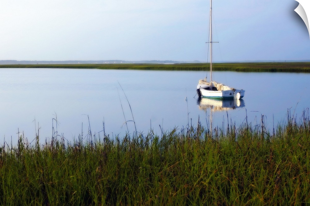 A landscape photograph of a sailboat anchored in still waters surrounded by marshy grasses on the shore.