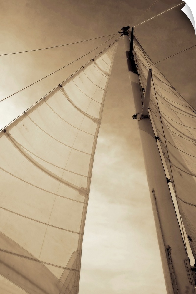 Vertical, low angle photograph, looking up large sails as the sun shines through them, against a partly cloudy sky.