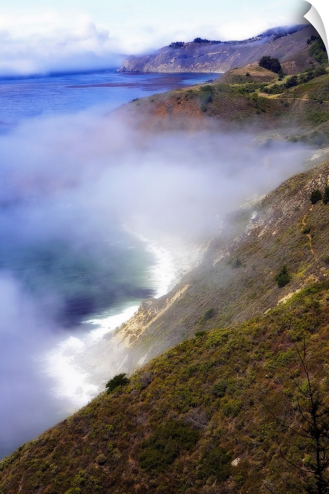 Photograph of fog rolling in off the California Big Sur ocean hitting the cliffs of the mountains that line the coast.
