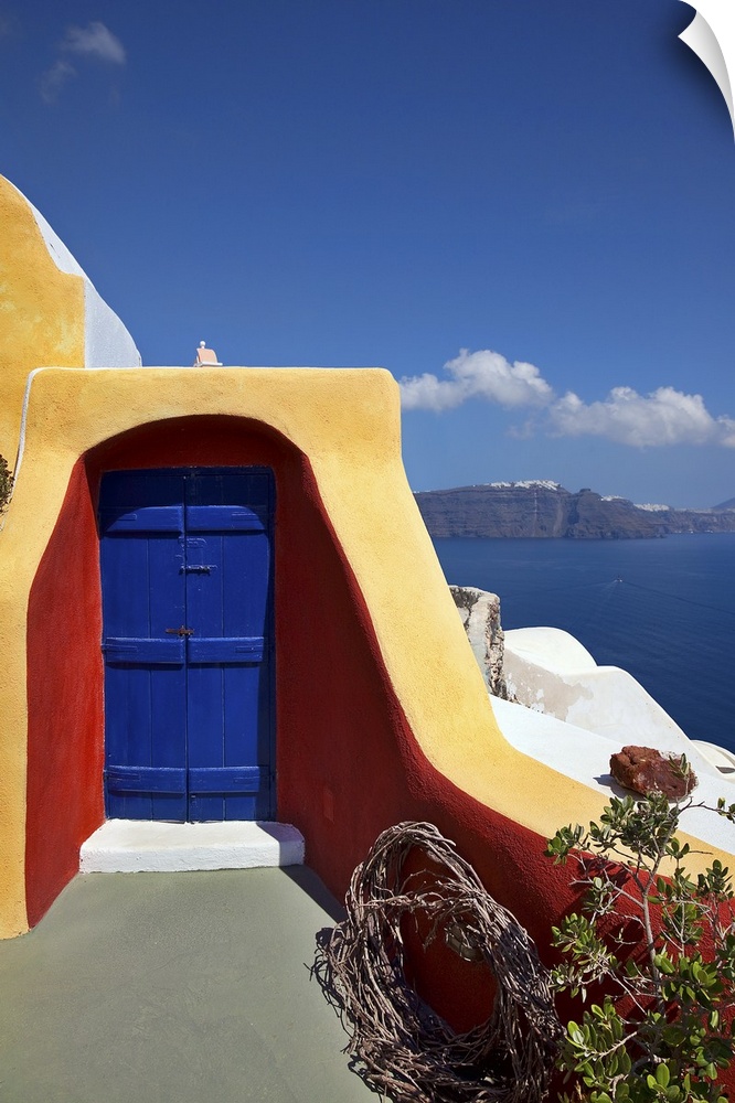 Close up vertical of deck with blue door and orange and red siding and ocean view in the village of Oia in Santorini, Greece