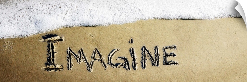 The word "Imagine" drawn in the sand near the ocean water.