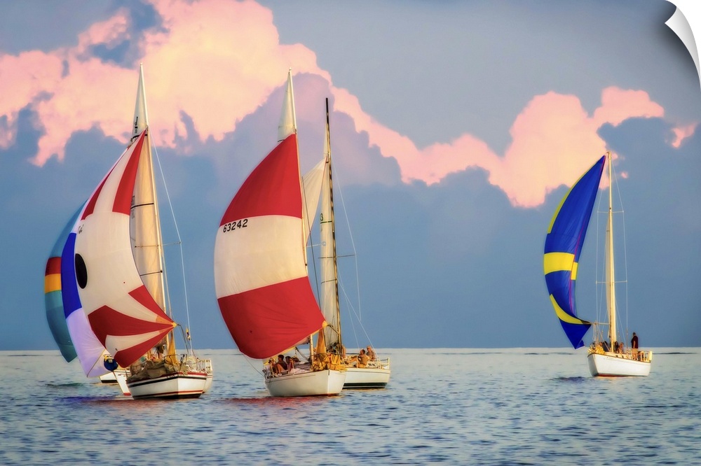 Sailboats with colorful sails on the water with large clouds in the sky.