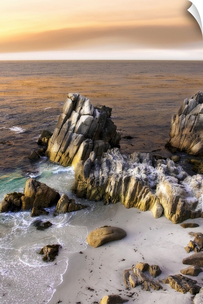 Vertical photo on canvas of tall rocks sticking out of the ocean by the shoreline with sun set warmed clouds in the sky.