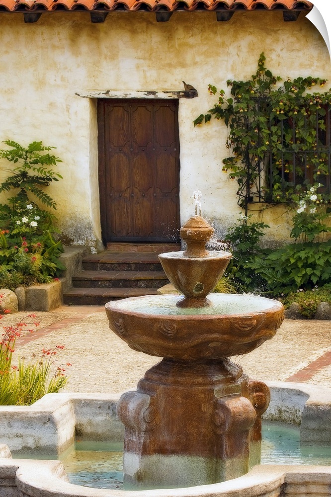 Photograph taken of a fountain sitting in front of a home with steps leading up to a wooden door. Foliage sits to either s...