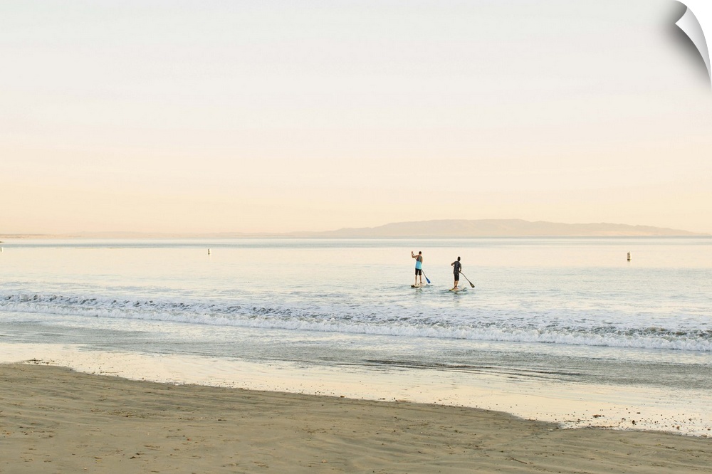 Two paddleboarders in the ocean, seen from the shore.