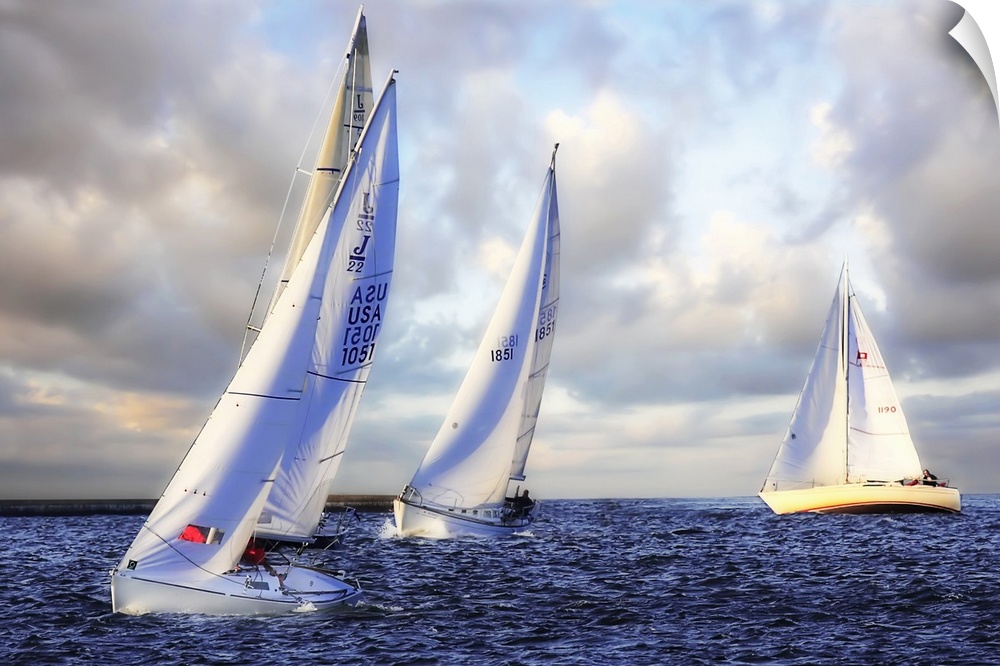 Several sail boats are pictured in open water and the sky filled with grey clouds.