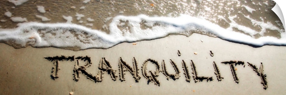 The word "Tranquility" drawn in the wet sand near ocean water.