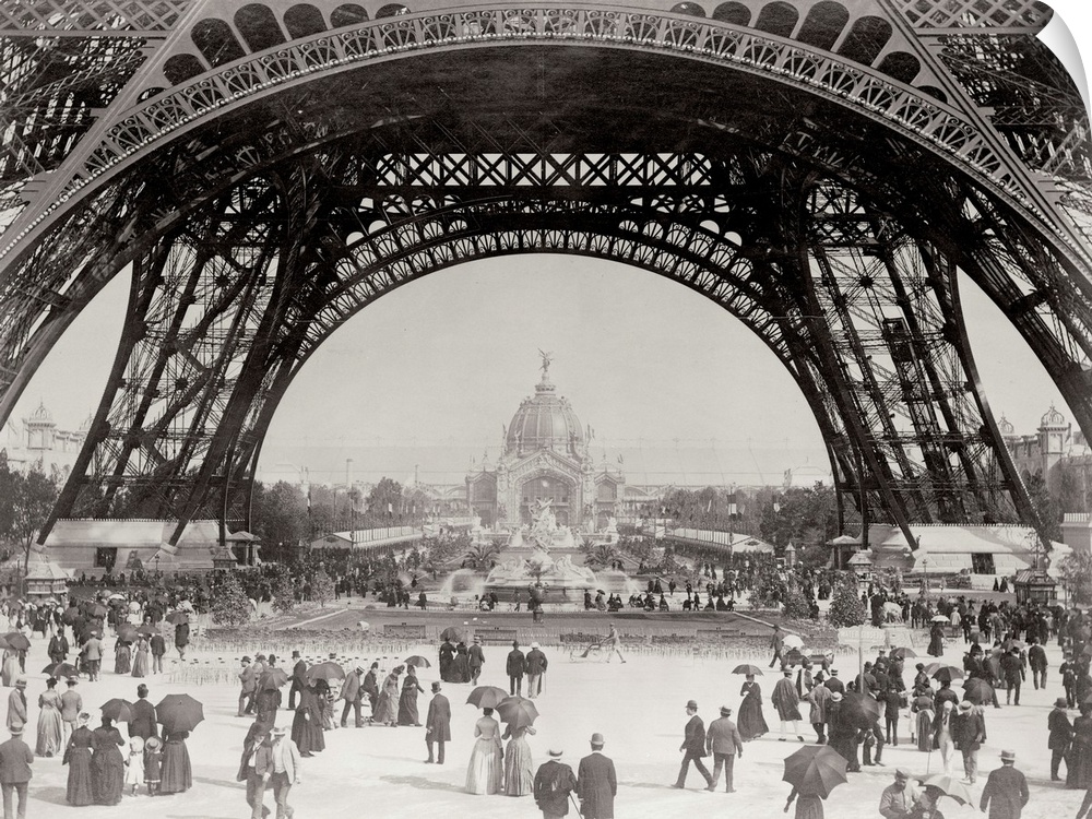 Vintage photograph of people standing under the base of the Eiffel Tower in Paris.