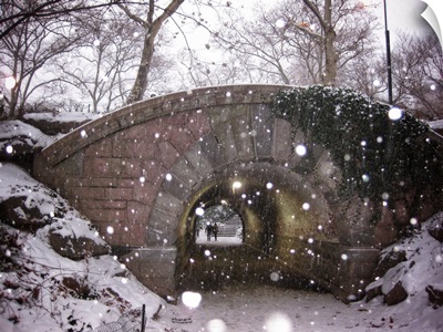 A couple walking under a bridge in New York City's Central Park on a snowy winter day.
