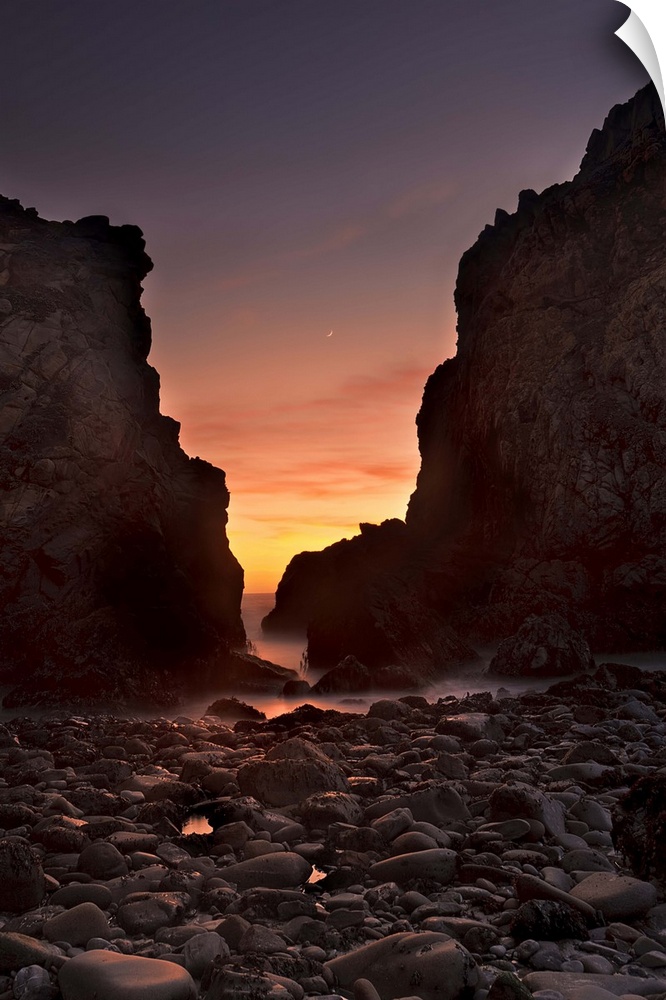 A crescent moon sets through a dusk-colored sky at Pfeiffer Beach, Big Sur, California, USA.