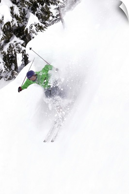 A free skier skis down a steep hill near trees, kicking up snow.