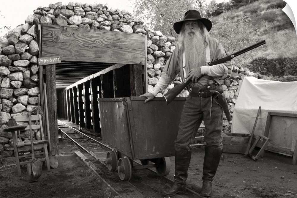 Old bearded man, a gold digger in front of a mine with a gun