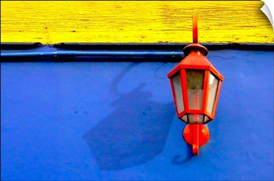 A red streetlamp on a blue and yellow wall.