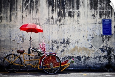 A traditional penang trishaw sits in front of an old weathered wall