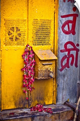 a yellow mailbox is draped with red flowers were left over from a puja