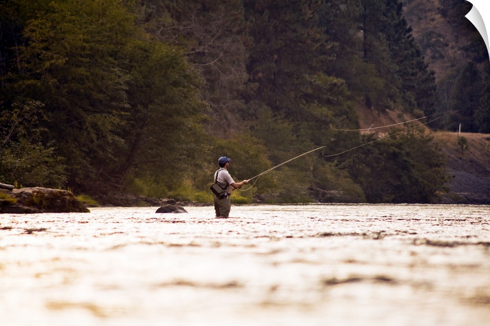 A fisherman standing in a river practicing his craft at sunset.