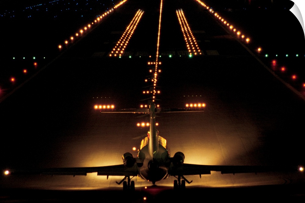 Giant photograph shows a small aircraft stationed at the end of a brightly lit airstrip at nighttime.