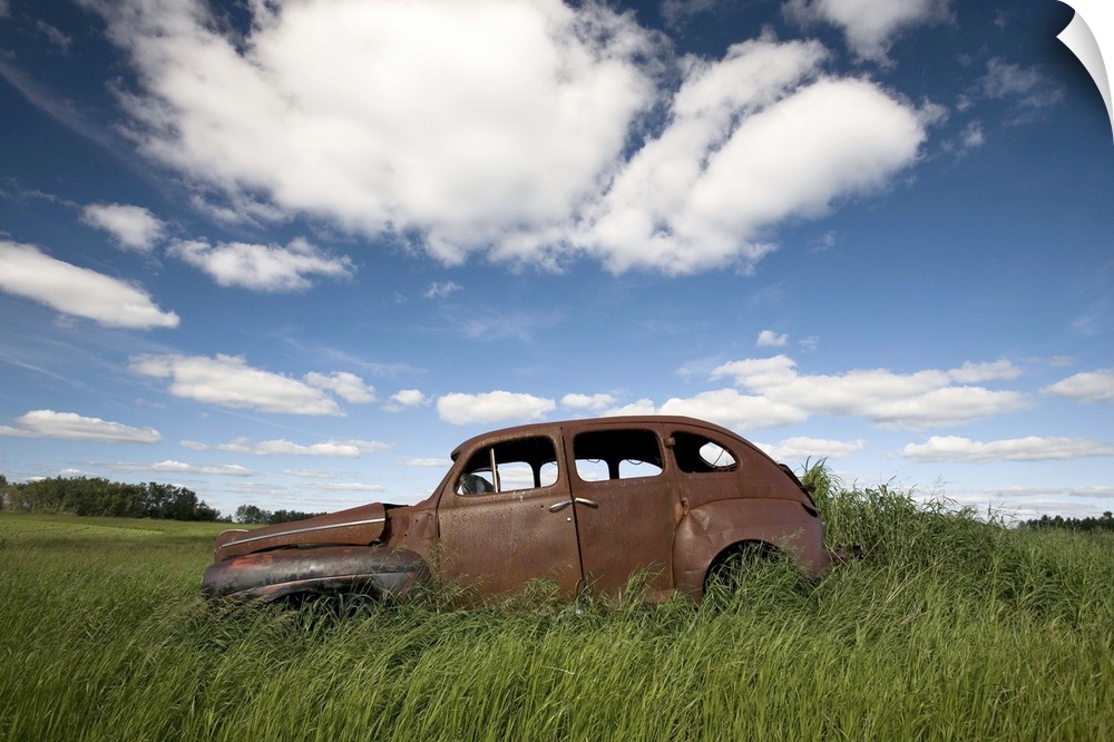 An abandoned classic car in a prairie field