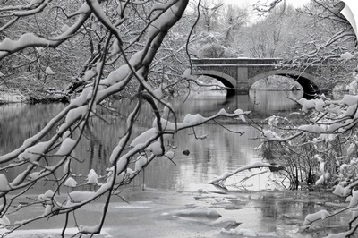 Arch bridge over partially frozen river seen trough snow covered branches.