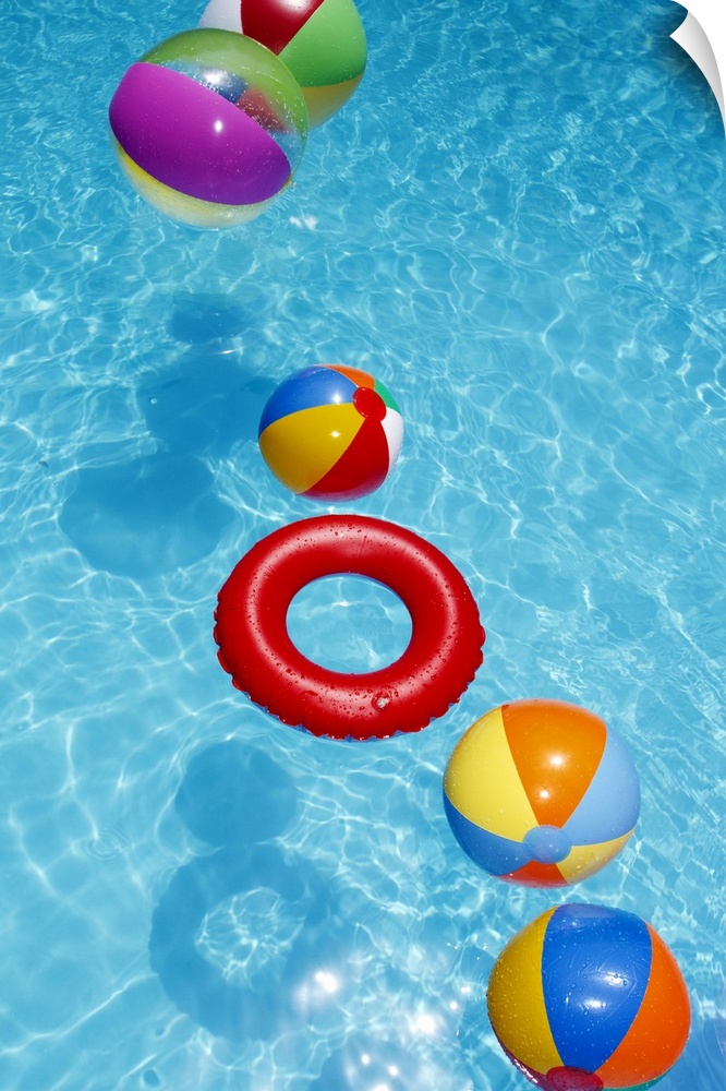 Beachballs blowing in wind in sparkling blue swimming pool.