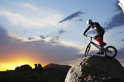 Bike rider balancing on rock boulder, side view